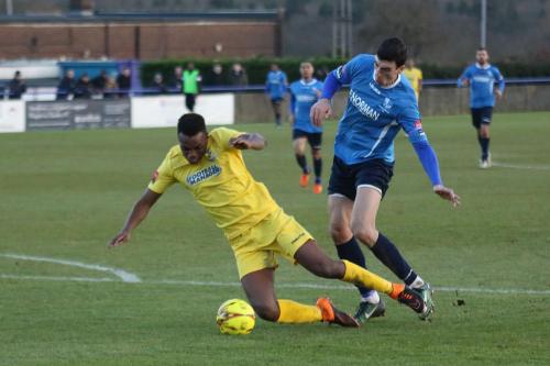 Wingates Claudiu Vilcu (blue) brings down Karl Oliyide to concede a penalty and earn a yellow card