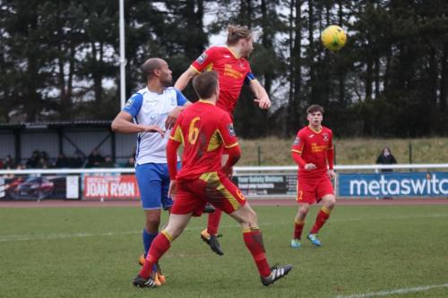 Needham captain Keiran Morphew heads clear from Simon Thomas (white)