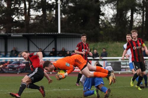 Brightlingsea keeper James Bradbrook saves from Dernell Wynter as Jake Gould covers