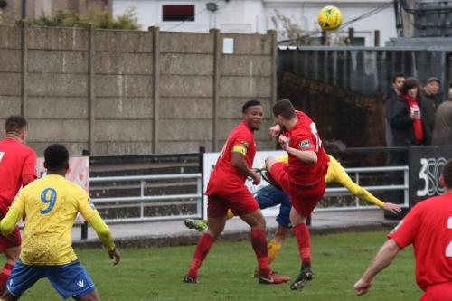Harrows Michael Bryan (red, R) clears as captain Shaun Preddie looks on