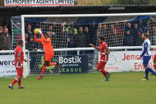 Merstham keeper Amadou Tangara collects the ball after a mistimed header from Billy Bricknell (R)