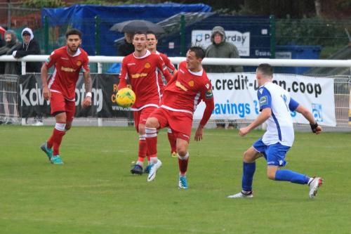 Mersthams Jake Hutchings (red, R) clears from Brandon Adams