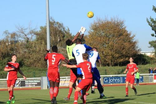 Whitehawk keeper Melvin Minter punches clear under pressure from Taofiq Olomowewe (white 5) and Billy Bricknell
