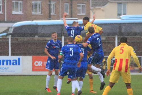 Enfields Rian McLean (yellow) challenges at a set piece during a heavy rain shower