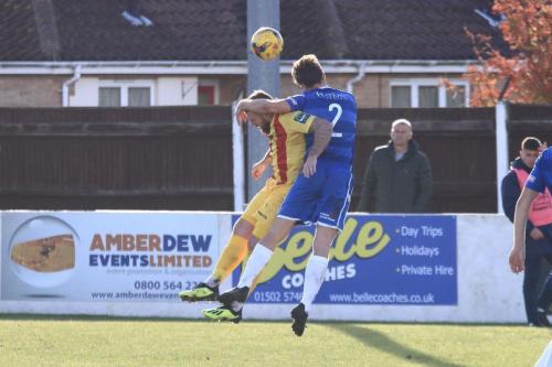 Lowestofts Adam Tann (blue) wins a header against Billy Bricknell