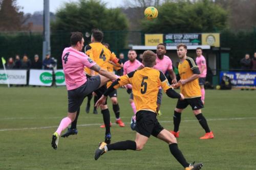 Mersthams Simon Cooper (amber 4) gets his head to the ball ahead of Enfields Matt Johnson (pink 4)