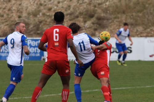 Whitehawks Yannis Ambroisine (red, R) heads clear from Sam Youngs