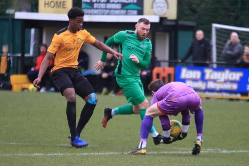 Merstham keeper Matte Pierson just beats Billy Bricknell to the ball as Emmanuel Fernandez (L) covers